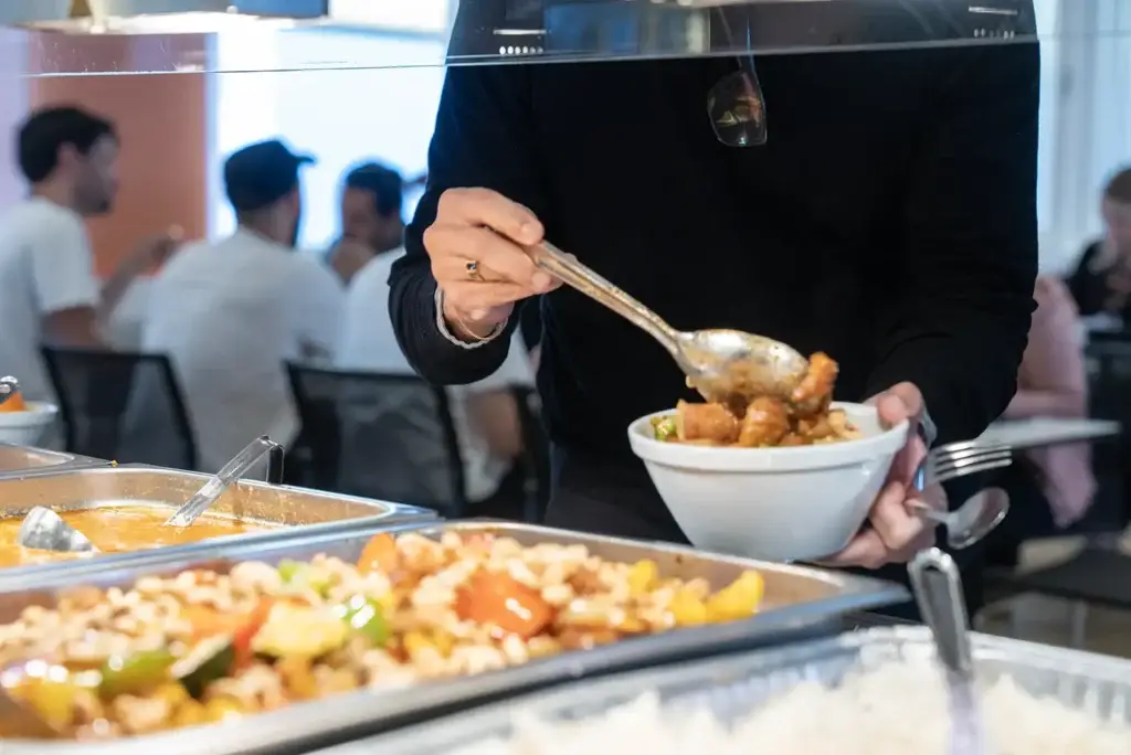 En dame som forsyner seg av varmmat i en kantine