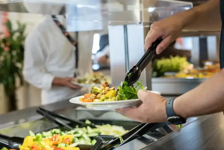 Nærbilde av hender som forsyner seg med mat i Løvetann Kantine