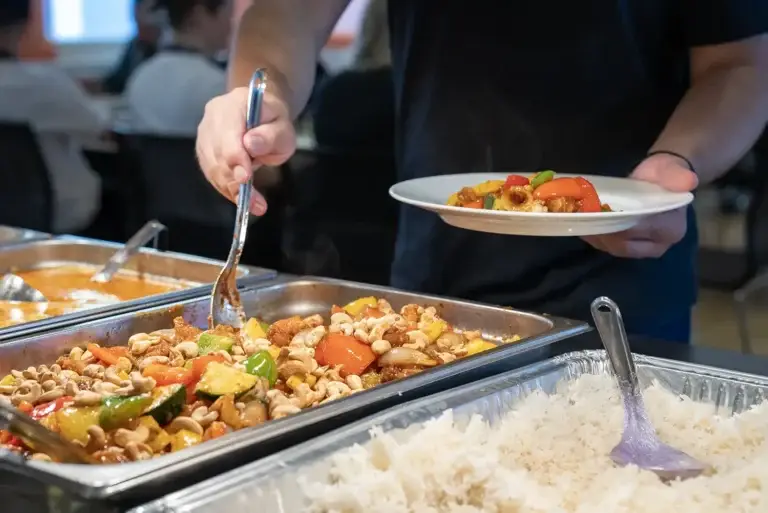 Nærbilde av hender som forsyner seg av varmrett i en kantine
