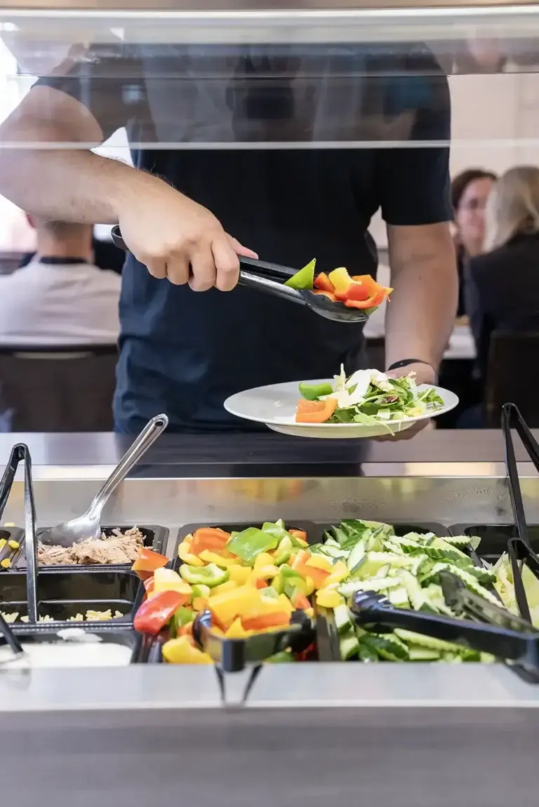 Person som legger paprika i salaten i Løvetann Kantine